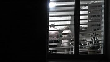 Peeping. Voyeur. Neighbor pervert Voyeur in evening on street looks out window as bare super-sexy neighbor in kitchen preps dinner for her husband. bare in public. bare at home. Family.  Outdoor